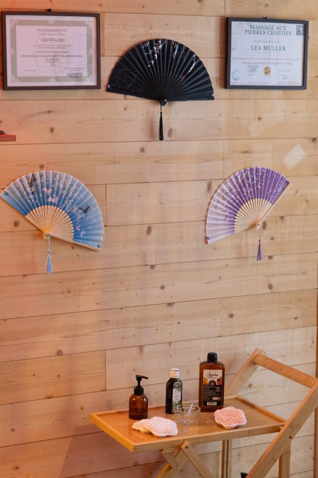 Détail du cabinet : éventails décoratifs, certificats de réflexologie et table d'huiles essentielles.